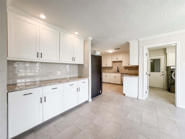 kitchen with light stone counters, washer / dryer, freestanding refrigerator, decorative backsplash, and white cabinets