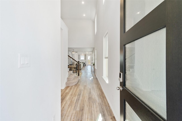 hallway featuring a high ceiling, stairs, light wood-type flooring, and baseboards