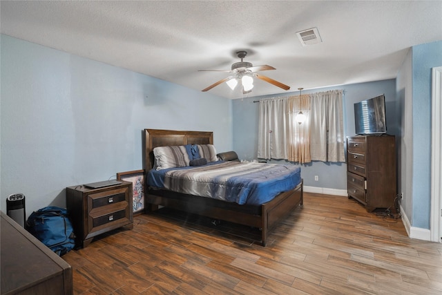 bedroom with visible vents, baseboards, wood finished floors, a textured ceiling, and a ceiling fan