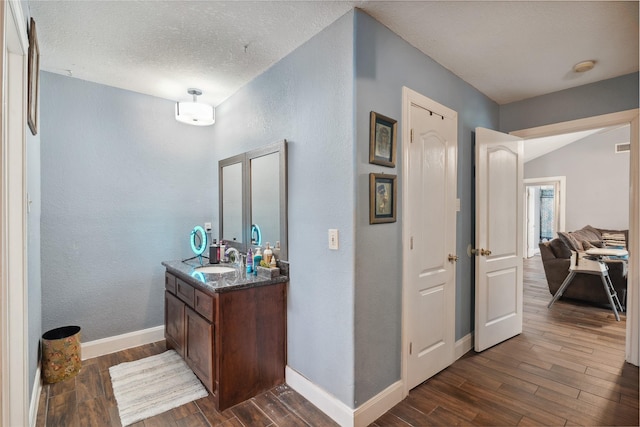 interior space featuring vanity, wood finished floors, baseboards, a textured ceiling, and a textured wall