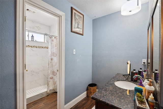 full bath featuring baseboards, tiled shower, a textured wall, and wood finished floors