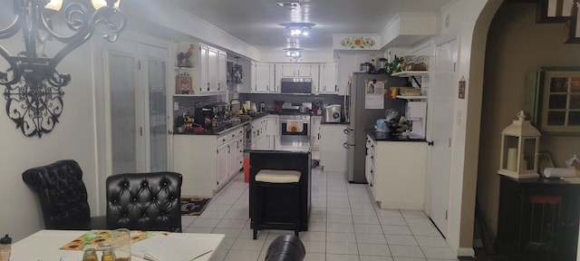 kitchen with dark countertops, arched walkways, appliances with stainless steel finishes, white cabinets, and light tile patterned floors