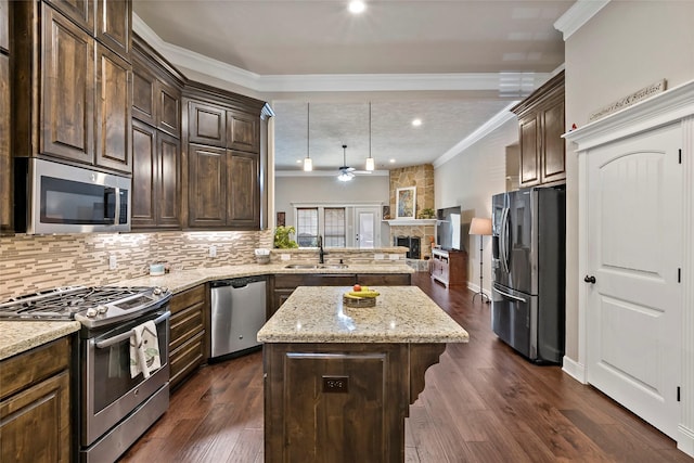 kitchen with ornamental molding, a sink, a center island, appliances with stainless steel finishes, and a fireplace