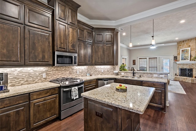 kitchen featuring dark wood finished floors, ornamental molding, appliances with stainless steel finishes, a peninsula, and a sink