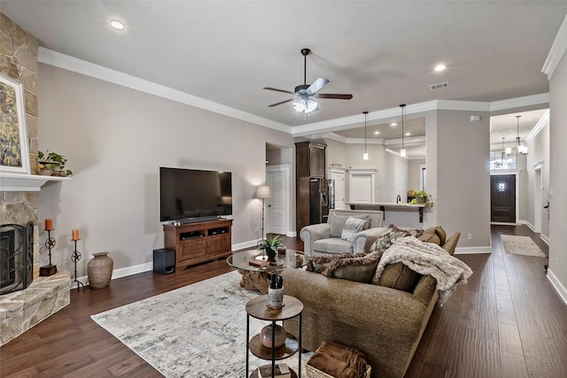 living area featuring visible vents, a stone fireplace, ornamental molding, and dark wood-style flooring