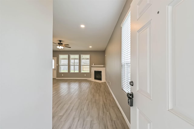 unfurnished living room with a fireplace with flush hearth, recessed lighting, light wood finished floors, baseboards, and ceiling fan