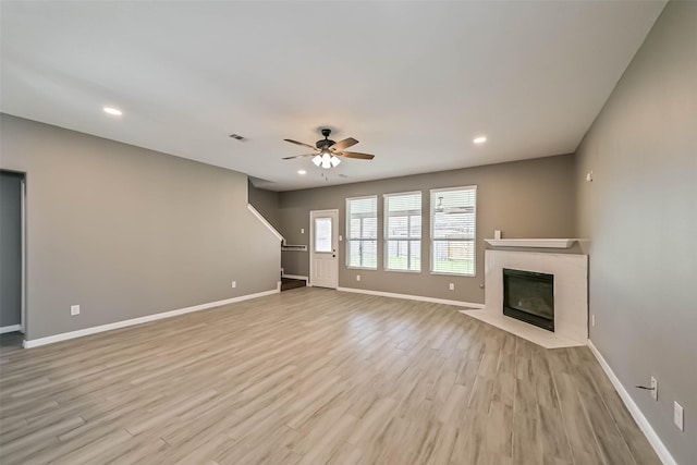 unfurnished living room with light wood finished floors, ceiling fan, baseboards, a fireplace with flush hearth, and recessed lighting