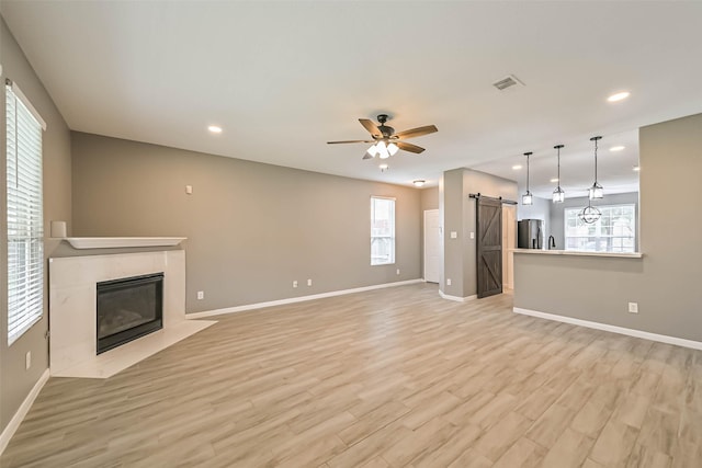 unfurnished living room featuring visible vents, a ceiling fan, a barn door, light wood-style floors, and a premium fireplace