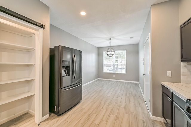 kitchen with light wood-type flooring, a barn door, an inviting chandelier, stainless steel fridge with ice dispenser, and light stone countertops