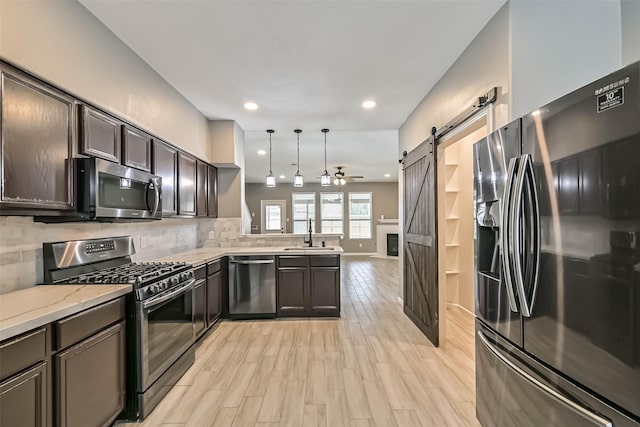 kitchen featuring light wood-style flooring, backsplash, stainless steel appliances, a barn door, and a peninsula