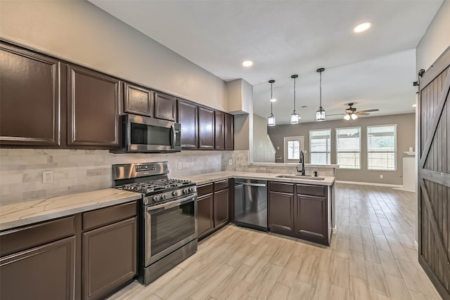 kitchen featuring dark brown cabinets, backsplash, a barn door, appliances with stainless steel finishes, and a sink