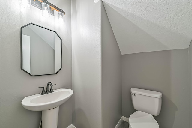 bathroom with toilet, lofted ceiling, and a sink