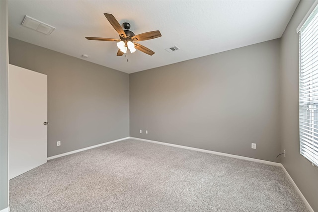 carpeted empty room featuring visible vents, a ceiling fan, and baseboards