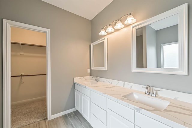 bathroom with double vanity, a walk in closet, baseboards, and a sink