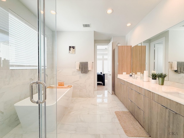 ensuite bathroom featuring a soaking tub, recessed lighting, tile walls, marble finish floor, and connected bathroom