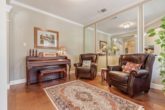 living area featuring visible vents, crown molding, decorative columns, and hardwood / wood-style floors