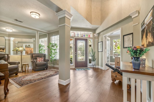 foyer featuring wood-type flooring, a healthy amount of sunlight, visible vents, and ornate columns