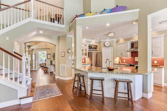 kitchen with hardwood / wood-style floors, arched walkways, high end fridge, ornamental molding, and wall chimney range hood