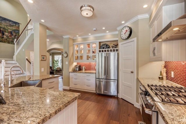 kitchen with a sink, dark wood-style floors, arched walkways, appliances with stainless steel finishes, and wall chimney range hood