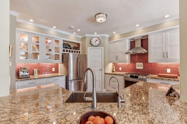 kitchen with light stone countertops, stainless steel appliances, white cabinets, glass insert cabinets, and wall chimney range hood