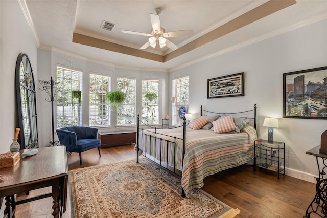 bedroom featuring visible vents, crown molding, a tray ceiling, and wood-type flooring