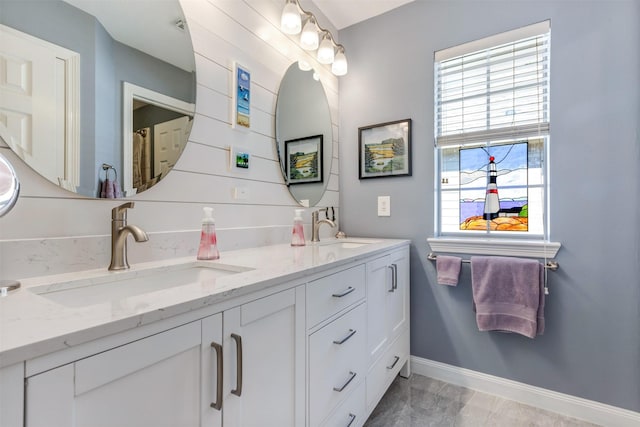 full bath featuring double vanity, baseboards, and a sink