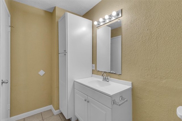 bathroom with vanity, tile patterned floors, a textured wall, and baseboards