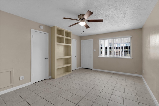 spare room with built in features, a textured ceiling, light tile patterned flooring, baseboards, and ceiling fan