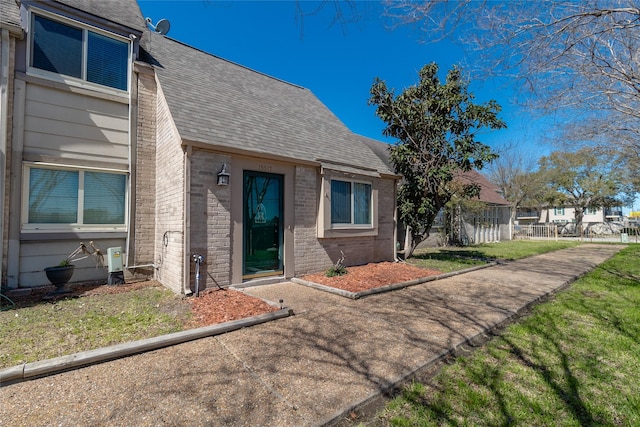 doorway to property with brick siding, a lawn, a shingled roof, and fence