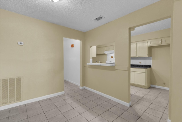 spare room featuring light tile patterned floors, visible vents, baseboards, and a textured ceiling