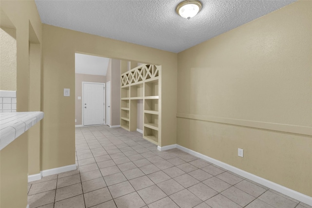 spare room with light tile patterned floors, baseboards, and a textured ceiling