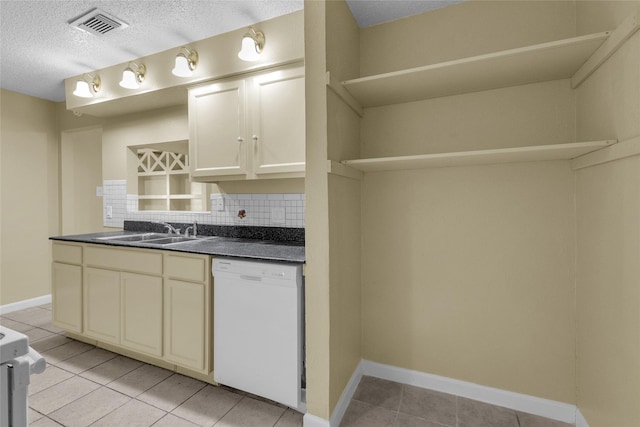 kitchen featuring visible vents, white dishwasher, a sink, dark countertops, and tasteful backsplash