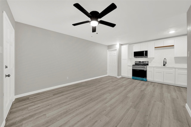 unfurnished living room featuring a sink, light wood-type flooring, baseboards, and ceiling fan