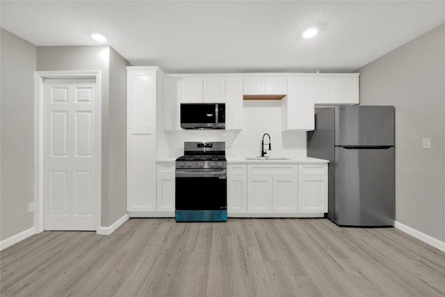 kitchen with white cabinets, stainless steel appliances, light countertops, and a sink