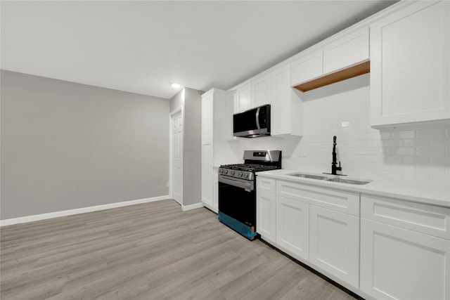 kitchen featuring light wood-type flooring, a sink, tasteful backsplash, appliances with stainless steel finishes, and baseboards