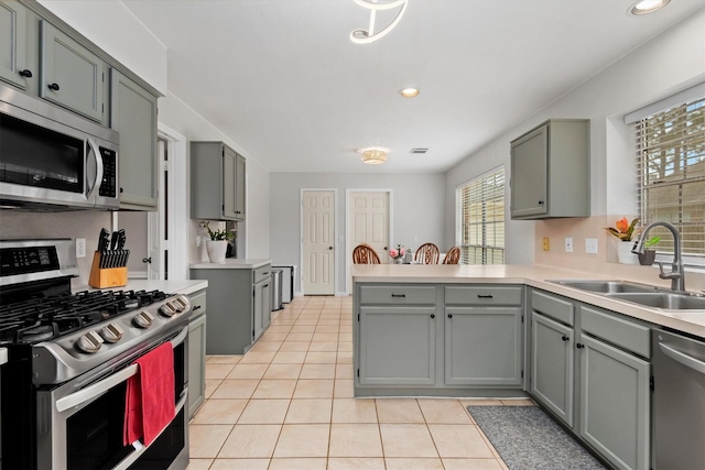 kitchen with gray cabinets, a sink, appliances with stainless steel finishes, a peninsula, and light tile patterned floors