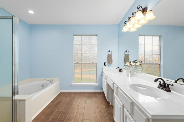 bathroom featuring wood finished floors, baseboards, double vanity, a sink, and a bath