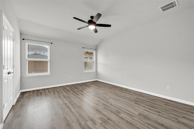 unfurnished room with vaulted ceiling, wood finished floors, visible vents, and baseboards