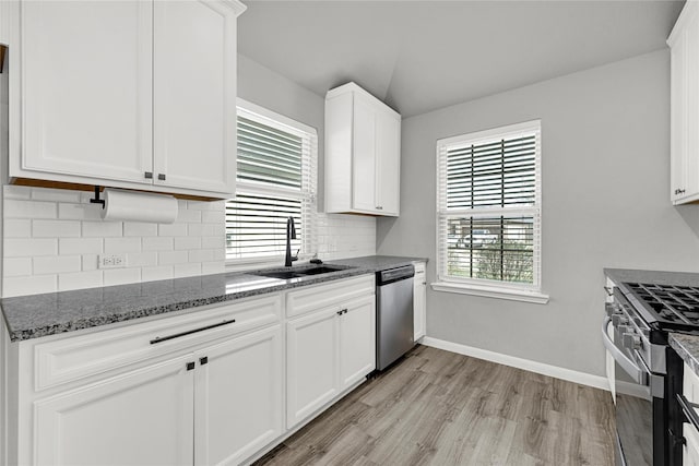 kitchen featuring a sink, dark stone countertops, white cabinetry, appliances with stainless steel finishes, and decorative backsplash