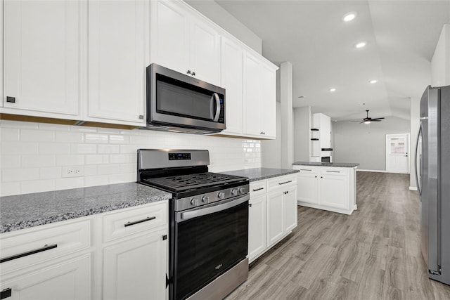 kitchen featuring dark stone counters, light wood-type flooring, lofted ceiling, stainless steel appliances, and white cabinetry