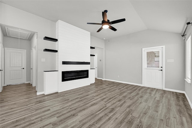 unfurnished living room with light wood finished floors, a large fireplace, ceiling fan, attic access, and vaulted ceiling