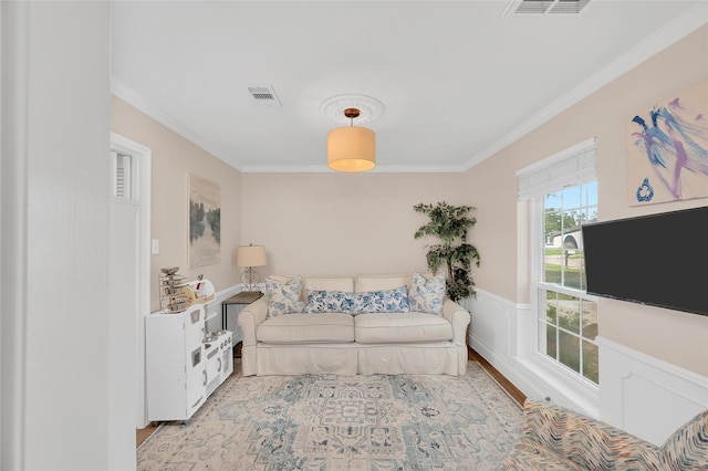 living room with visible vents, a wainscoted wall, and ornamental molding