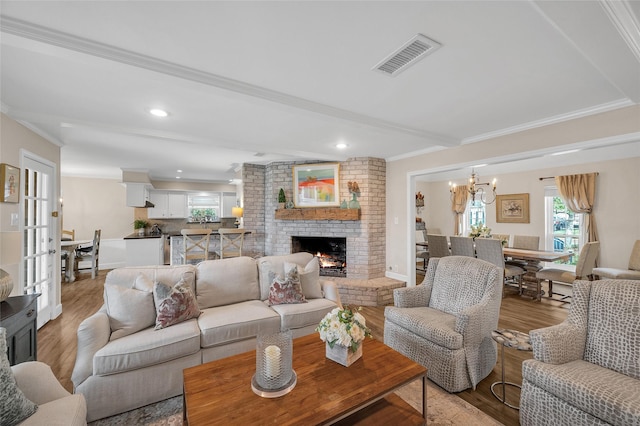 living room featuring visible vents, ornamental molding, light wood finished floors, a brick fireplace, and a chandelier