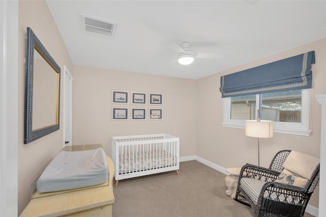 bedroom with carpet, visible vents, baseboards, ceiling fan, and a crib