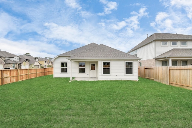 back of house with a fenced backyard, a shingled roof, and a yard