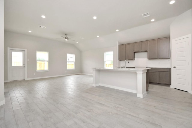 kitchen featuring visible vents, a center island with sink, a sink, vaulted ceiling, and light countertops