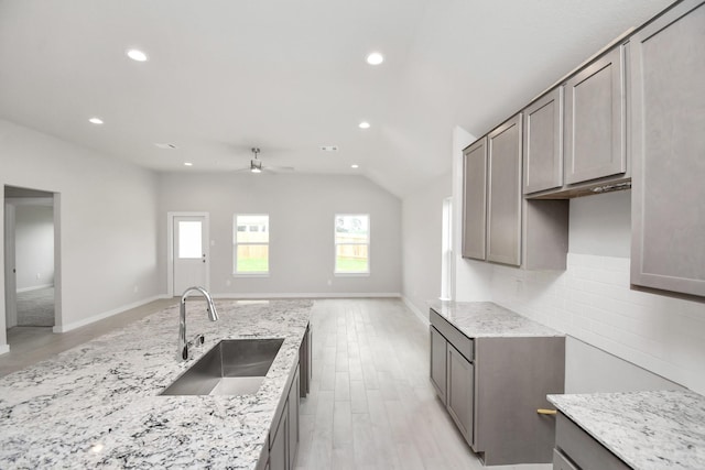 kitchen featuring light stone counters, open floor plan, decorative backsplash, and a sink