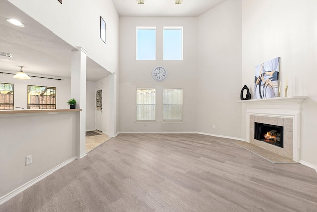 unfurnished living room with wood finished floors, visible vents, baseboards, a high ceiling, and a tiled fireplace