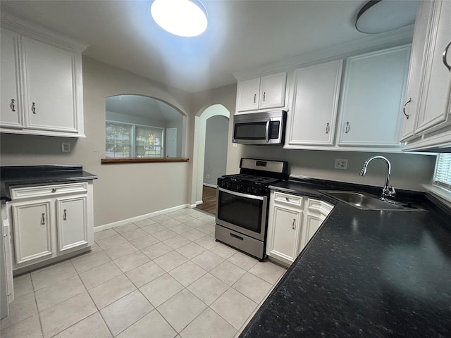 kitchen with a sink, stainless steel appliances, white cabinets, light tile patterned floors, and baseboards