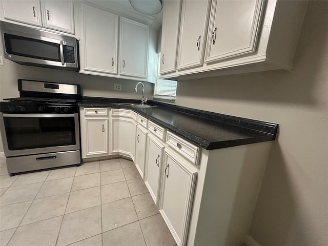 kitchen with dark countertops, light tile patterned floors, white cabinets, stainless steel appliances, and a sink